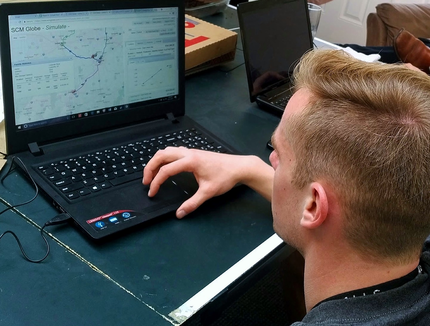 A picture of a blonde caucasian man working on a laptop displaying the SCM Globe app.