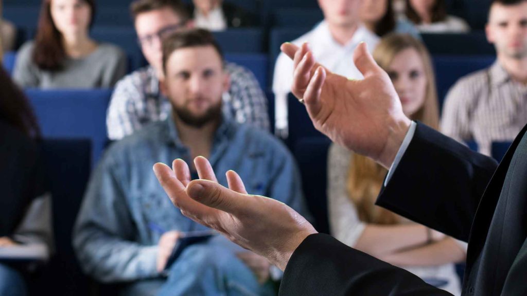 A picture focussing on the hands of a man speaking in front of people.